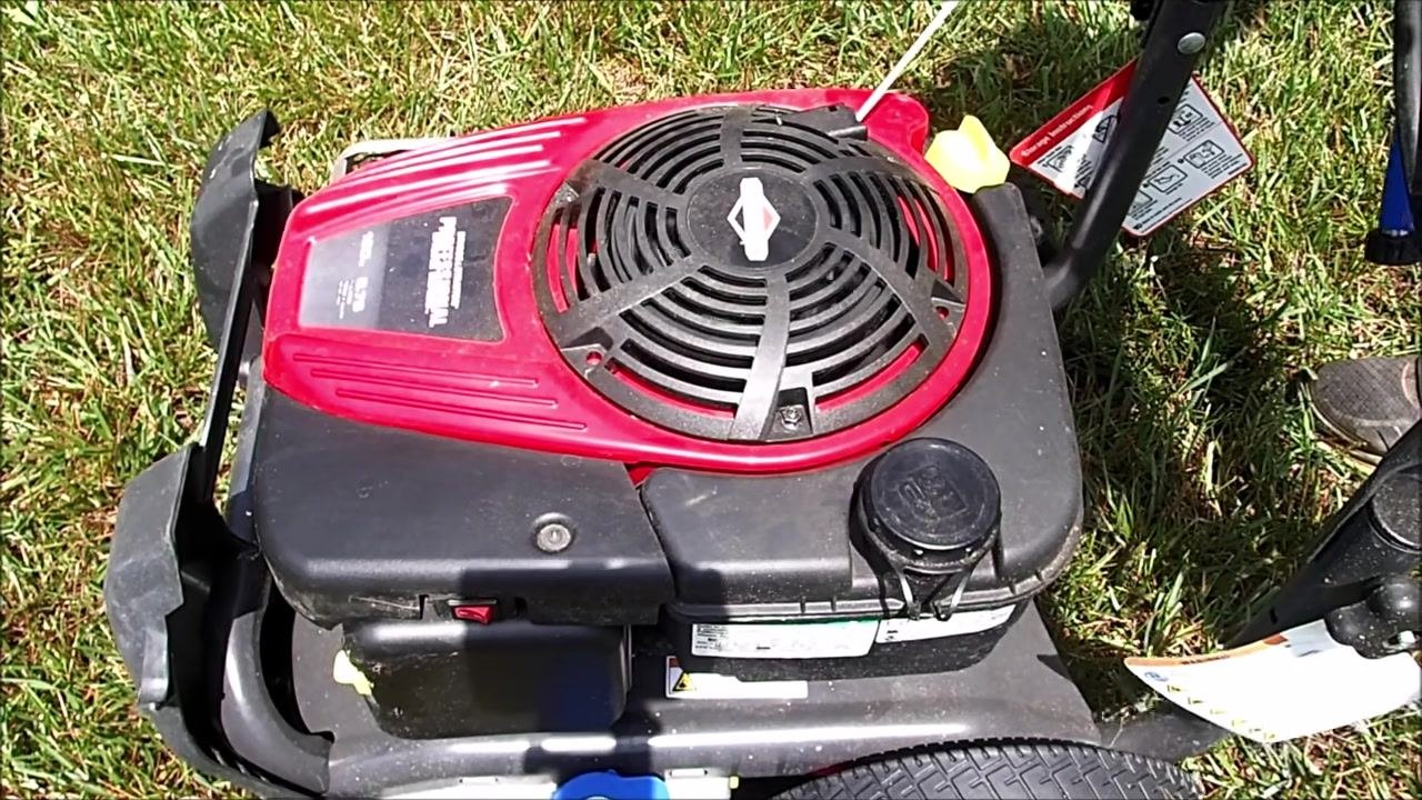 Close-up of a hand holding a can of carburetor cleaner and spraying into the air intake area, with the blue detergent cap and warning labels visible.
