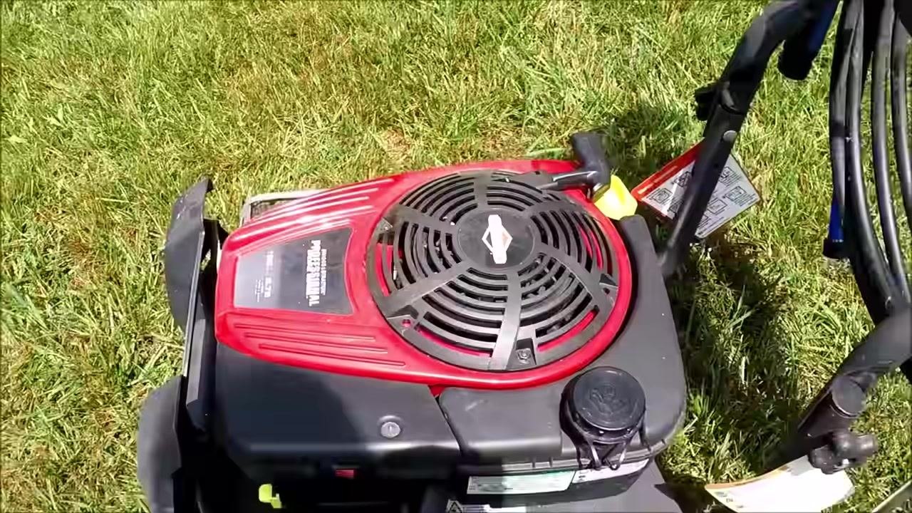 Top view of the pressure washer engine showing the red engine cover, pull handle, and fuel cap, with the starter cord in use on grass.