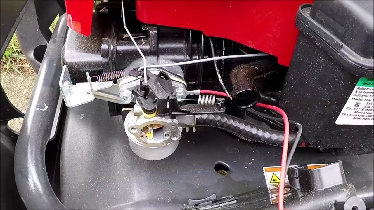 Carburetor still attached to the engine, with linkage, springs, red and black wires, an engine label, and surrounding components visible.