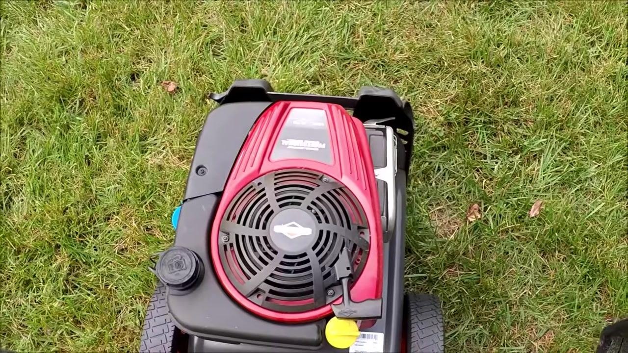 Close-up of the Briggs & Stratton engine, showing labels, switches, and caps on the power washer, with grass in the background.