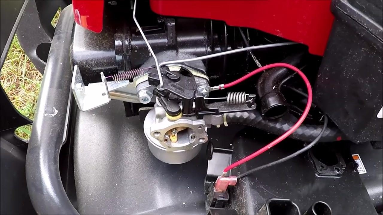 Hands holding the reassembled carburetor, pointing to the float mechanism and linkage to demonstrate float operation.