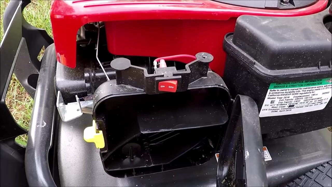 Close-up of the carburetor installed on the engine, focused on the linkage and spring connections, with the red wire and mounting bracket visible.