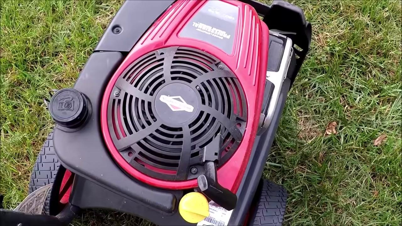 Engine top with the yellow oil fill cap, black fuel cap, red cover, and pull start handle on grassy ground.