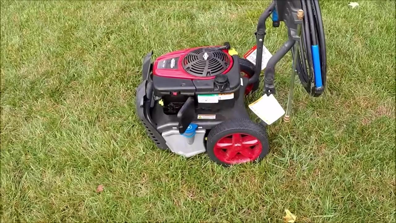 Power washer running on grass, hose coiled on handle, engine operating smoothly, wide view of the setup.