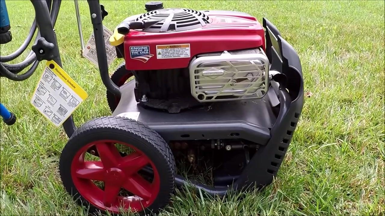 Side view of the power washer, focusing on the engine, wheels, and attached maintenance schedule tag.