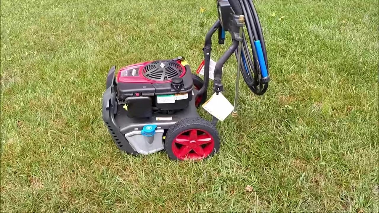 Close-up of a greasy foam air filter held in hand, with the pressure washer and grass in the background.
