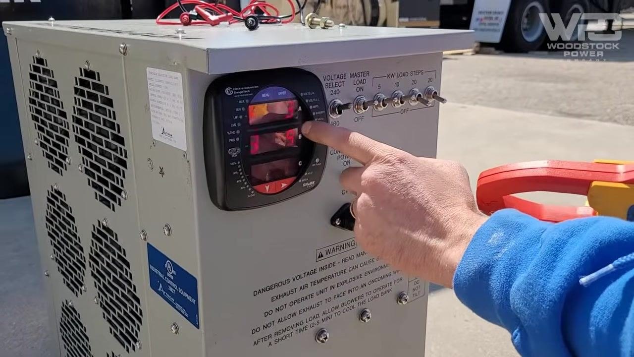 Technician adjusting load step switches on the load bank panel, with the digital ammeter displaying updated current values