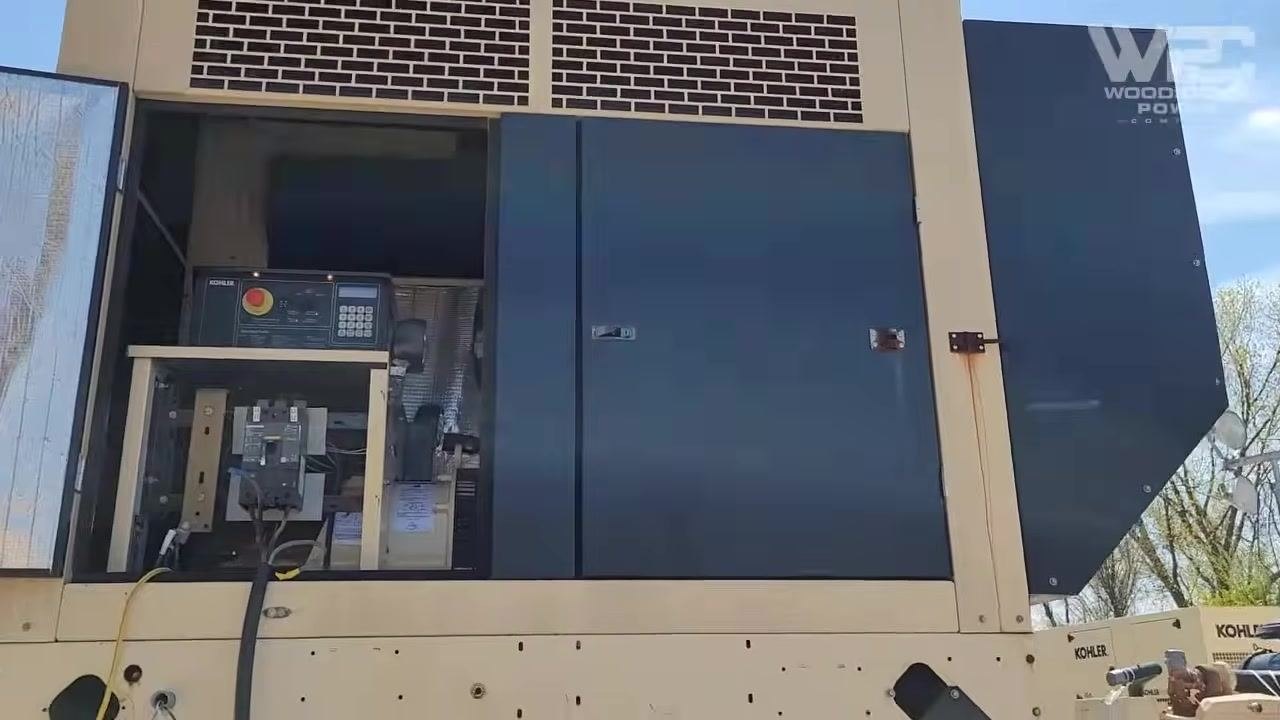 Wide view of the generator with the open control panel and breaker compartment, showing the emergency stop button and keypad, with the generator running outdoors