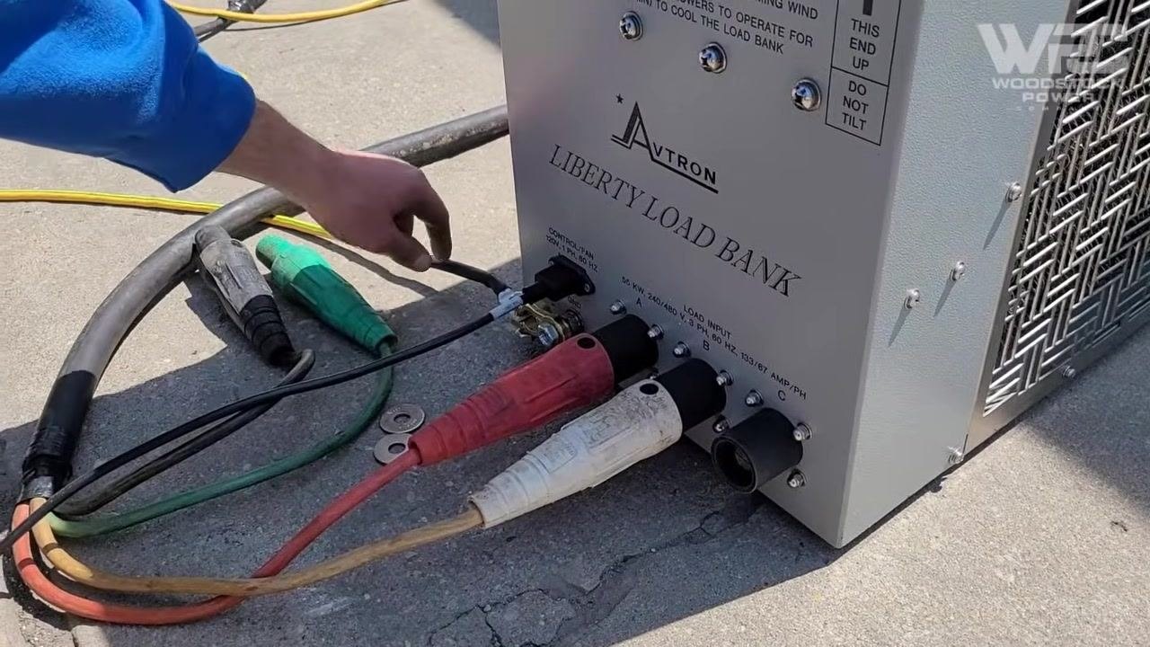 Close-up of the load bank showing multiple heavy-duty cables connected to labeled input terminals A, B, and C, the control fan power input, and the ground connection