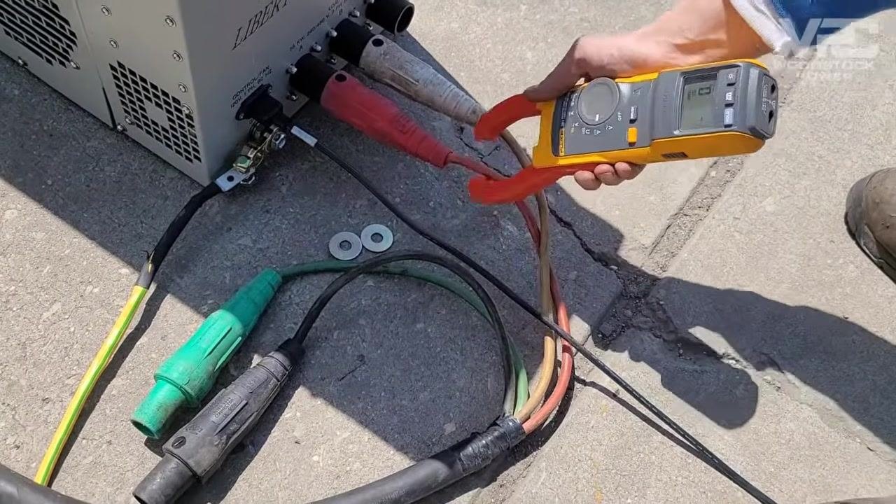 Technician using a clamp meter to measure current on individual leads connected to the load bank, with multiple heavy-duty cables and ground connections visible