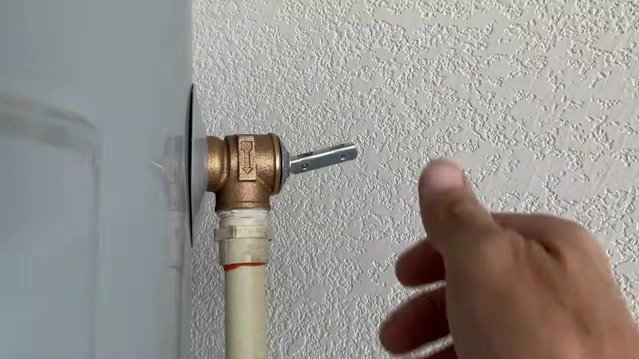 Hand reaching to close the brass drain valve on the water heater