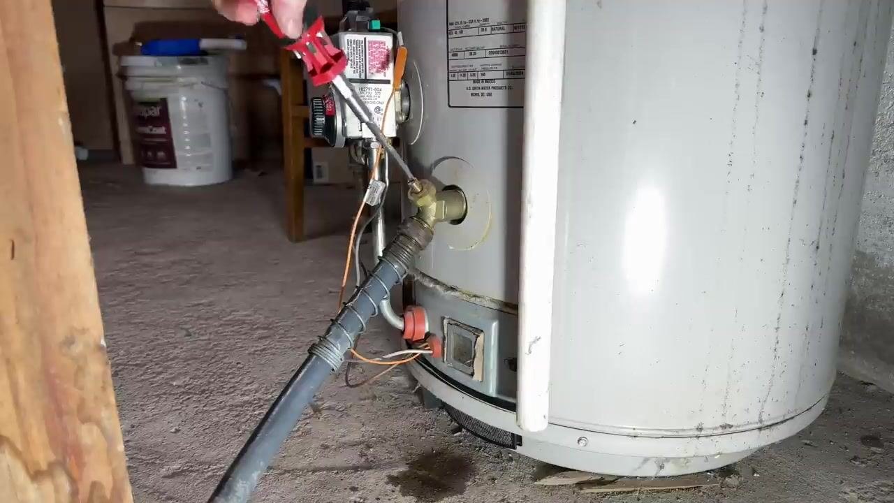 Close-up of a garden hose connected to the water heater's drain valve, being opened with a screwdriver.