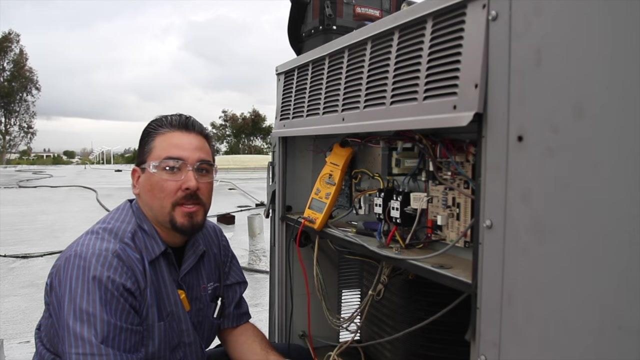 Technician using a multimeter set to microfarads to test the capacitor inside the open electrical compartment.