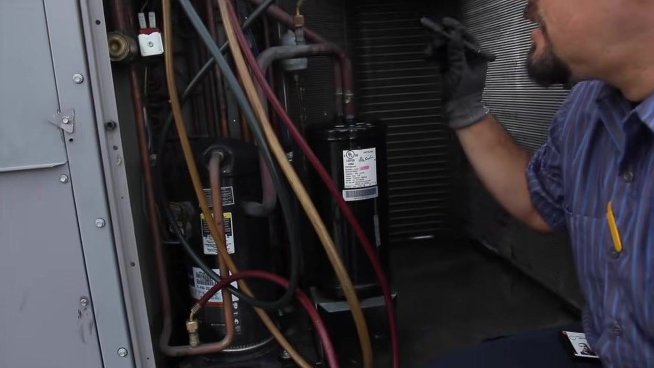 Technician referencing the compressor and electrical connections, preparing to check amp draws.