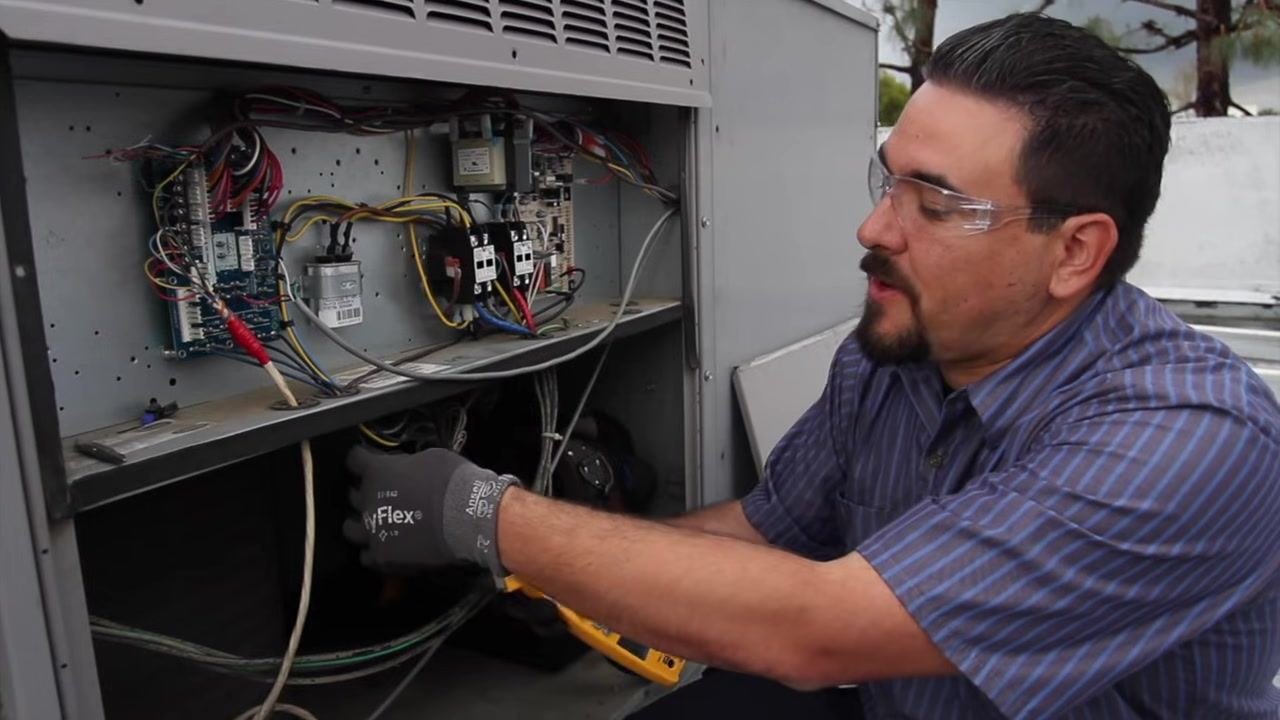 Technician reaching into the electrical compartment to measure condenser fan motor amperage.