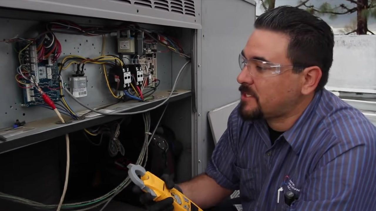 Technician confirming the condenser fan motor amperage reading inside the open electrical compartment.