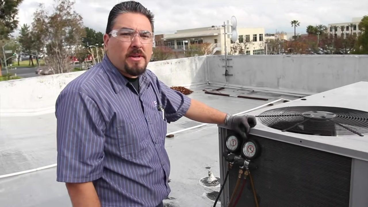 Technician using a clamp meter inside the open electrical compartment, preparing to check compressor amperage.