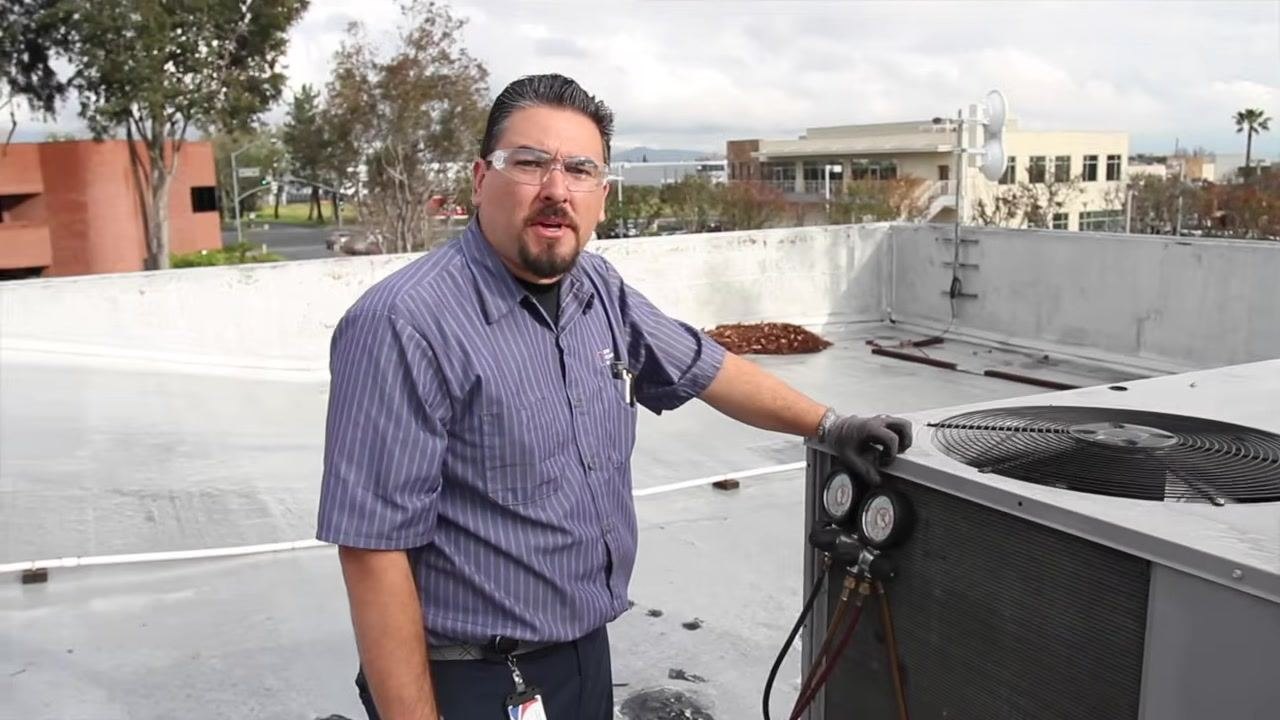 Technician holding a clamp meter, explaining blower motor amperage readings inside the open electrical compartment.