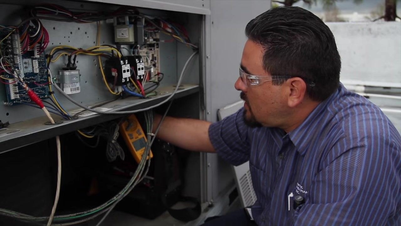 Technician measuring supply vent temperature at the labeled panel of the HVAC unit.
