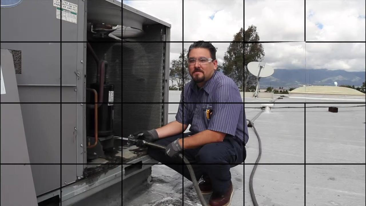 Technician kneeling by the open coil compartment, holding a water hose and preparing to clean the coil.