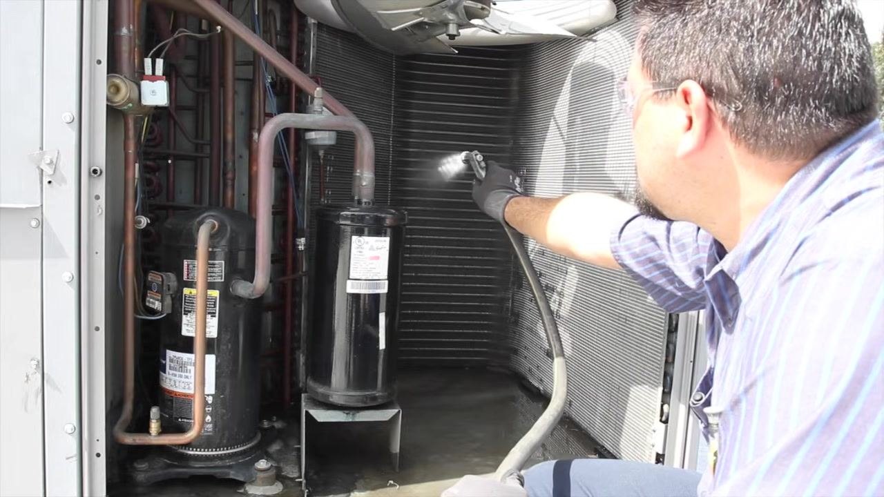 Technician using a screwdriver to check and tighten connections on a capacitor inside the open electrical compartment, with multiple colored wires, circuit boards, and a multimeter visible.