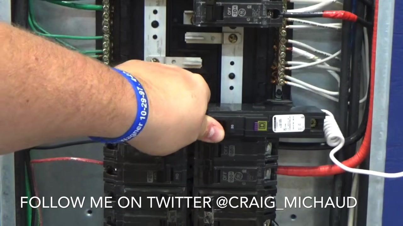 Hand pressing a circuit breaker firmly into place in the electrical panel, with multiple breakers, white and black wires, and the neutral/ground bar visible.