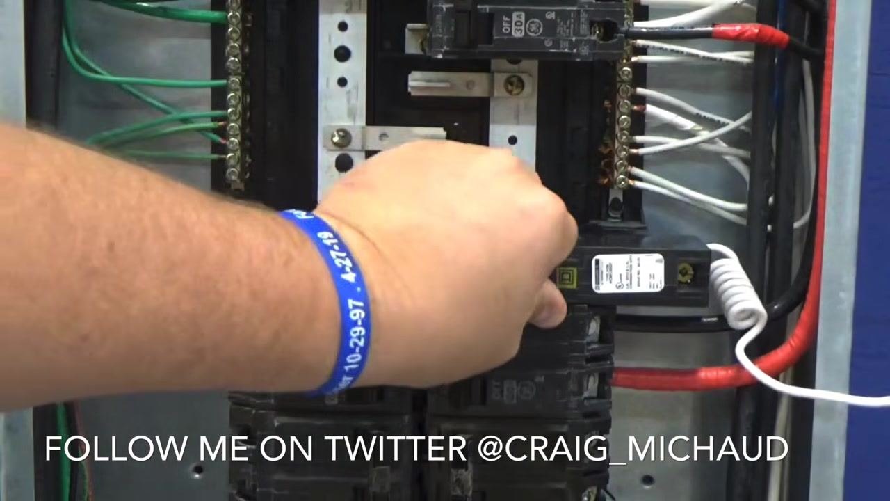 Hand using a screwdriver to tighten a screw on the neutral bar, securing the white wire alongside multiple other connected wires.