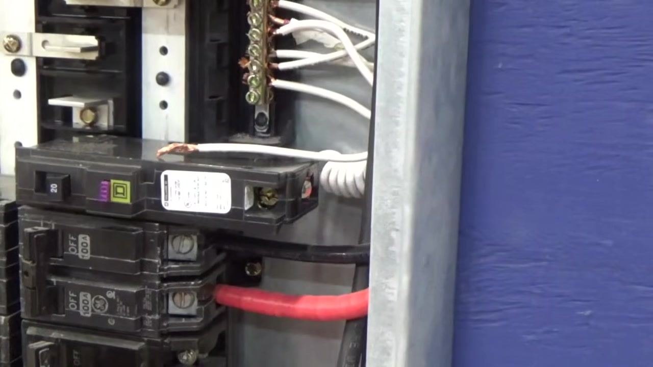 Breaker removed from the panel with the white coiled wire attached and its stripped end visible; the panel interior and other breakers are shown in the background.
