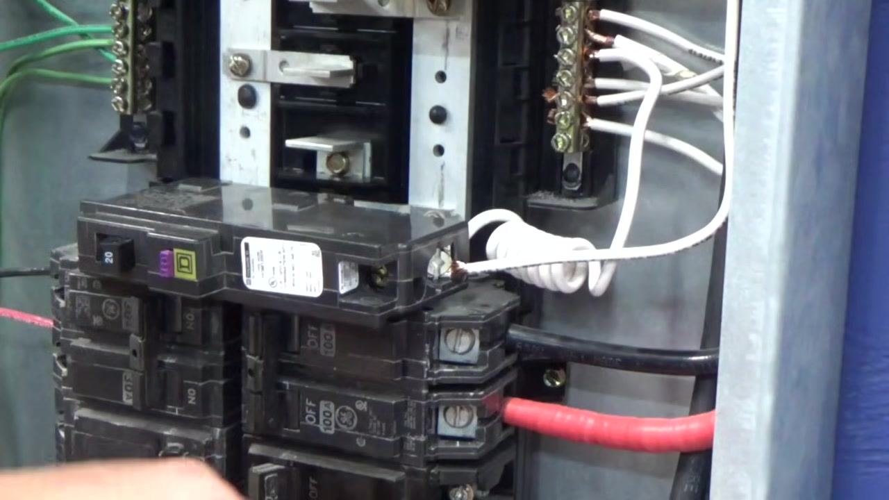Hands holding the breaker and the stripped white wire, preparing to insert the wire into the breaker terminal, with a screwdriver visible.