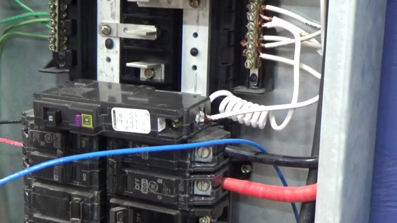 Close-up of the electrical panel showing the newly installed breaker with the white coiled wire attached and the blue wire ready to be connected.