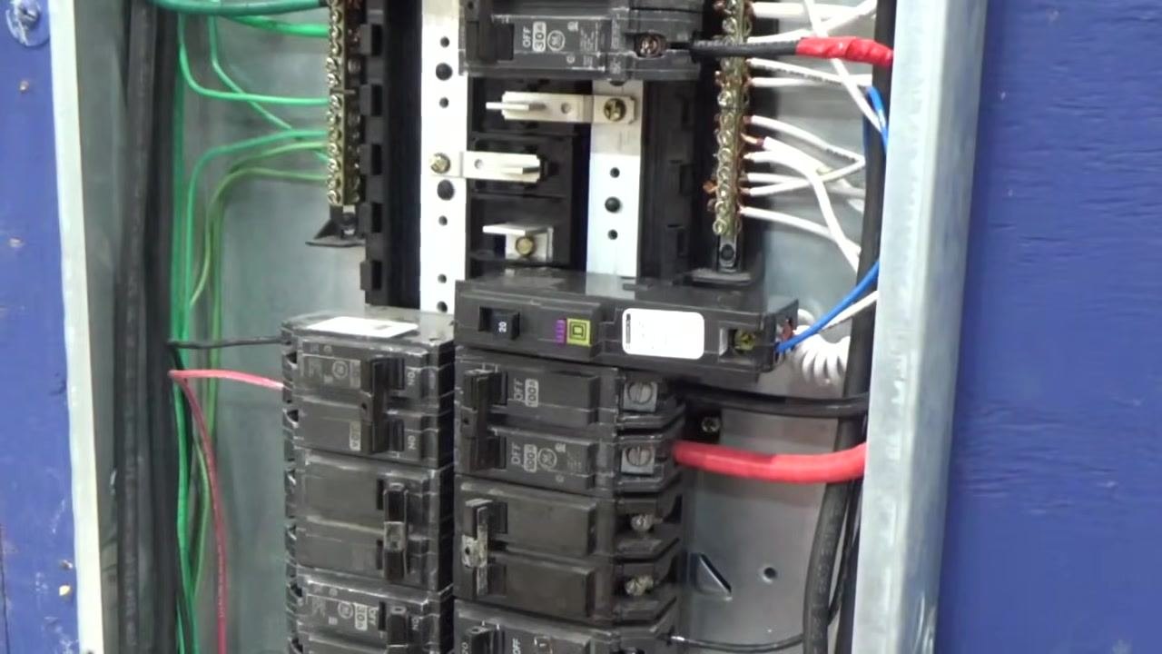 Hand holding the breaker with the blue and white wires attached, preparing to reinstall it into the panel.
