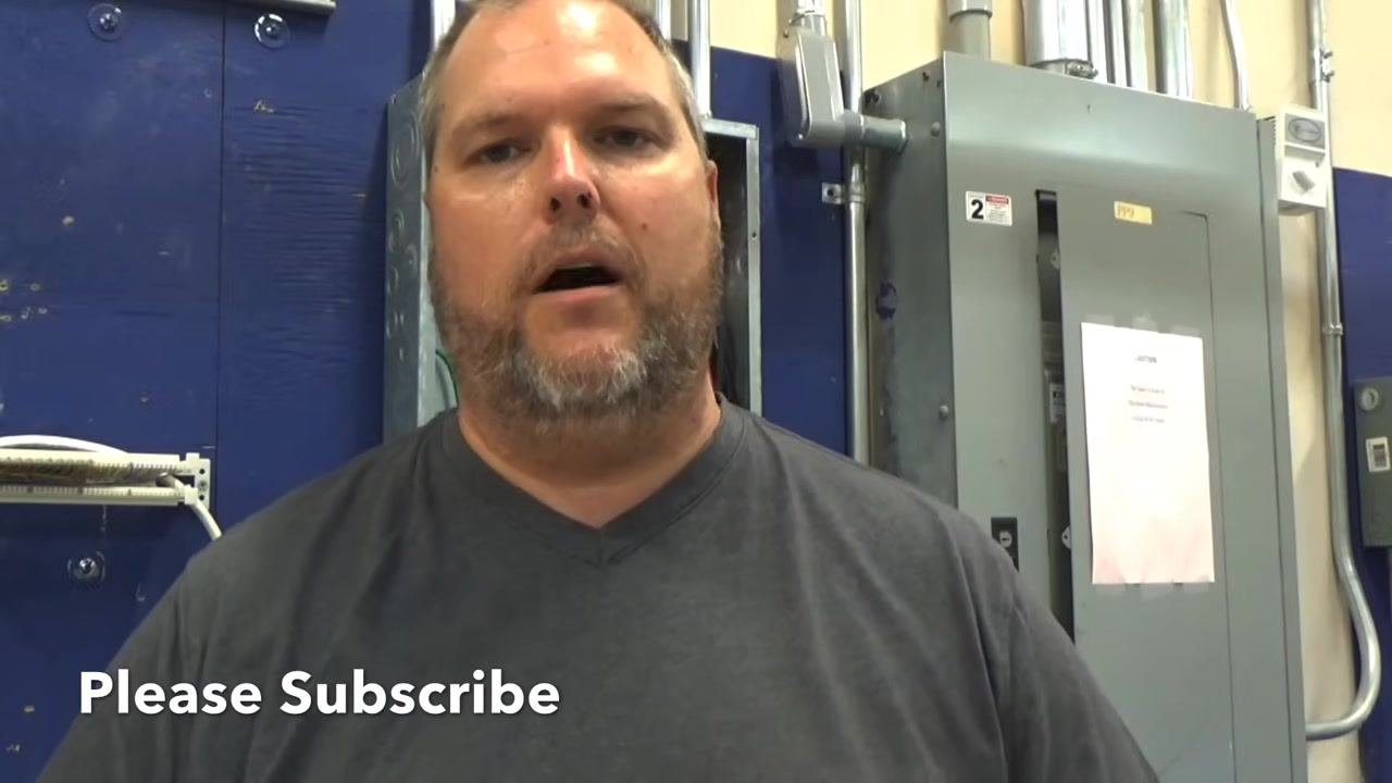 Instructor explaining the wiring process for a breaker, with the text 'Please Subscribe' overlaid. Electrical panels and conduit are visible in the background.