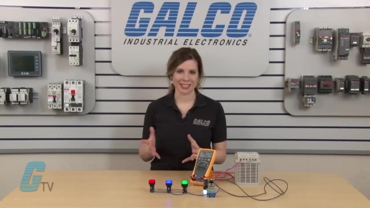 Presenter summarizing the demonstration, standing behind the setup with the multimeter, pilot lights, and power supply. The GALCO Industrial Electronics logo is visible in the background.