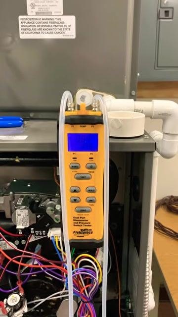 Manometer attached to the furnace, displaying a static pressure reading well over 1 inch, with the furnace open and wiring and tubing visible.