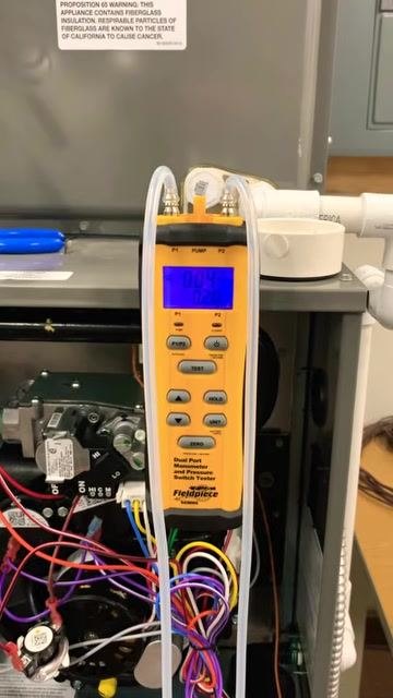 Manometer display showing a lower static pressure reading of 0.42 inches, indicating reduced resistance after the restriction is removed, with the furnace open and tubing and wiring visible.