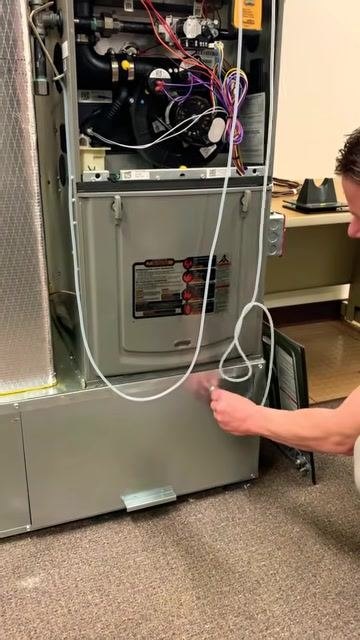Technician demonstrating the insertion of the supply side probe into the furnace, with the high limit switch removed and the probe placed into the opening left behind. The furnace is open, and the manometer tubing is visible.