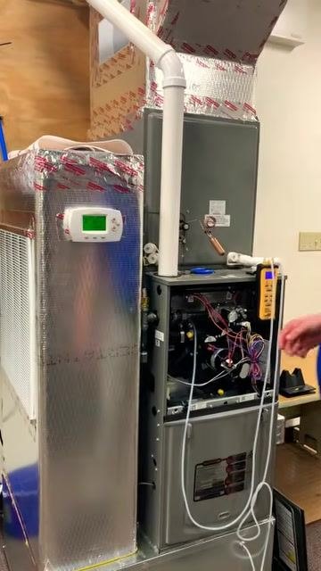 Technician reaching toward the furnace controls to turn on the blower fan, with the manometer attached and ready to display readings.