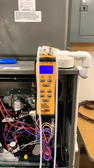 Close-up of the digital dual port manometer displaying the supply static pressure reading, with tubing connected and the display showing a value around 0.14 to 0.15 inches.