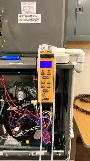 Digital manometer attached to the furnace, displaying static pressure readings with tubing connected to both ports, and the furnace wiring and components visible.
