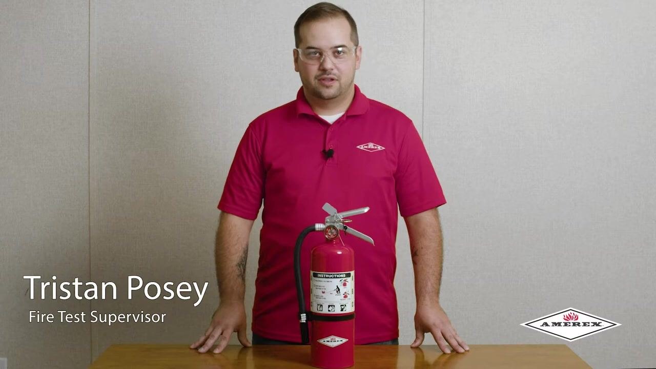 A fire extinguisher placed on a table, with a person standing behind it in a demonstration setting. The extinguisher is clearly visible and unobstructed.