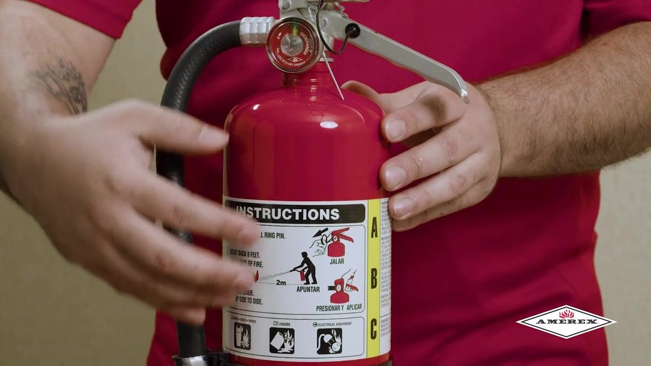 Close-up of hands holding the fire extinguisher, showing the instruction label and demonstrating how to heft or weigh the cylinder.