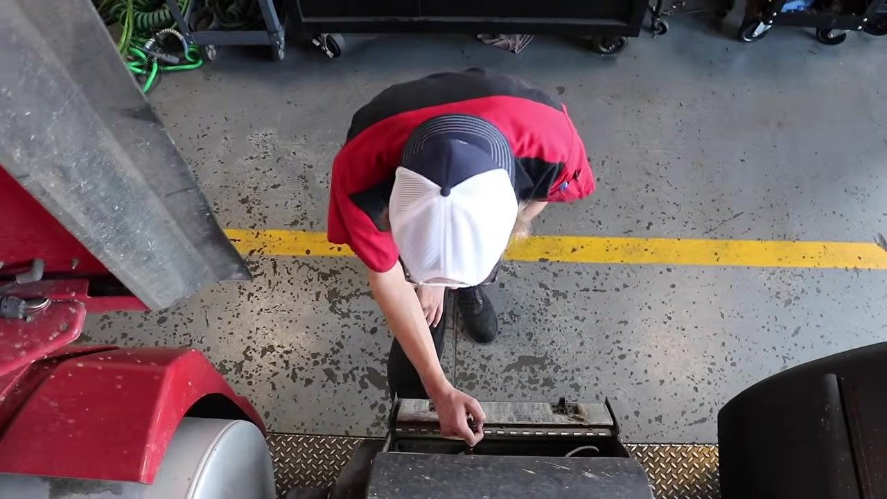 Close-up of the brake chamber, air hoses, and suspension components, with the mechanic's hand inspecting for leaks.
