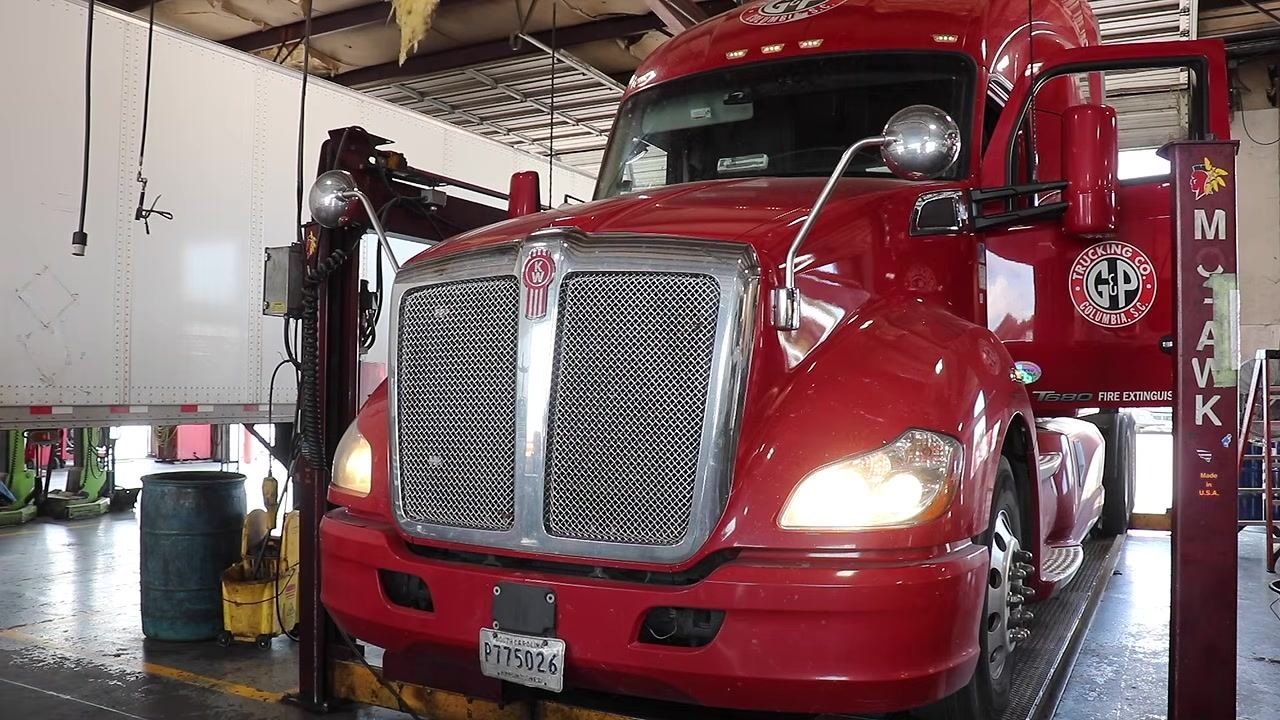 Front view of a red Kenworth truck with the left headlight illuminated and the right headlight out.