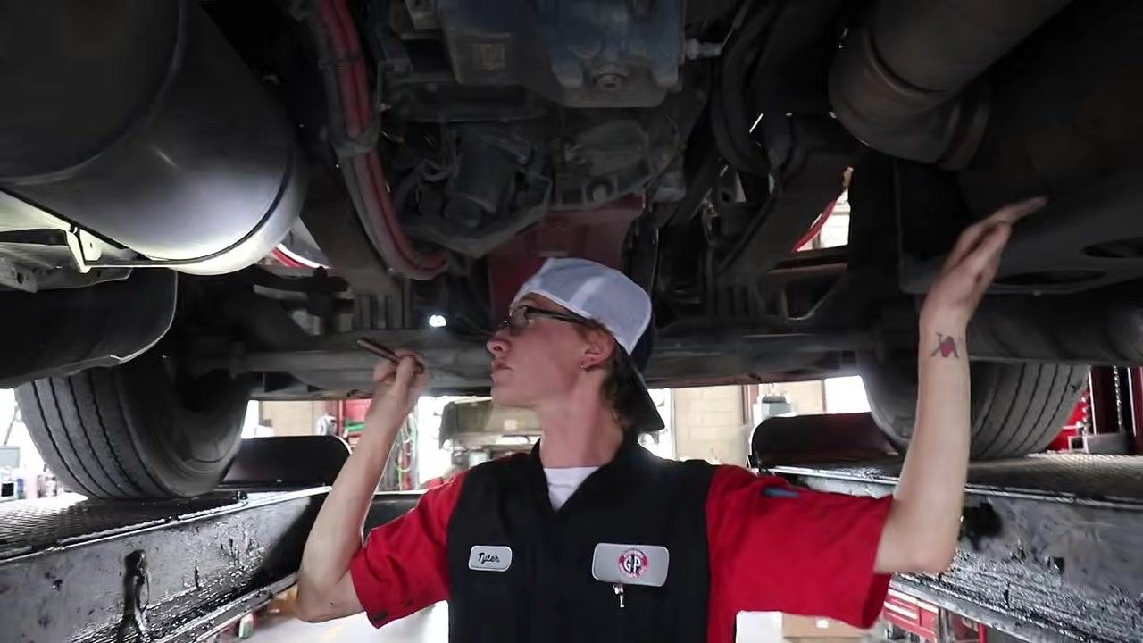 Technician under the truck, inspecting suspension and structural components with a flashlight.