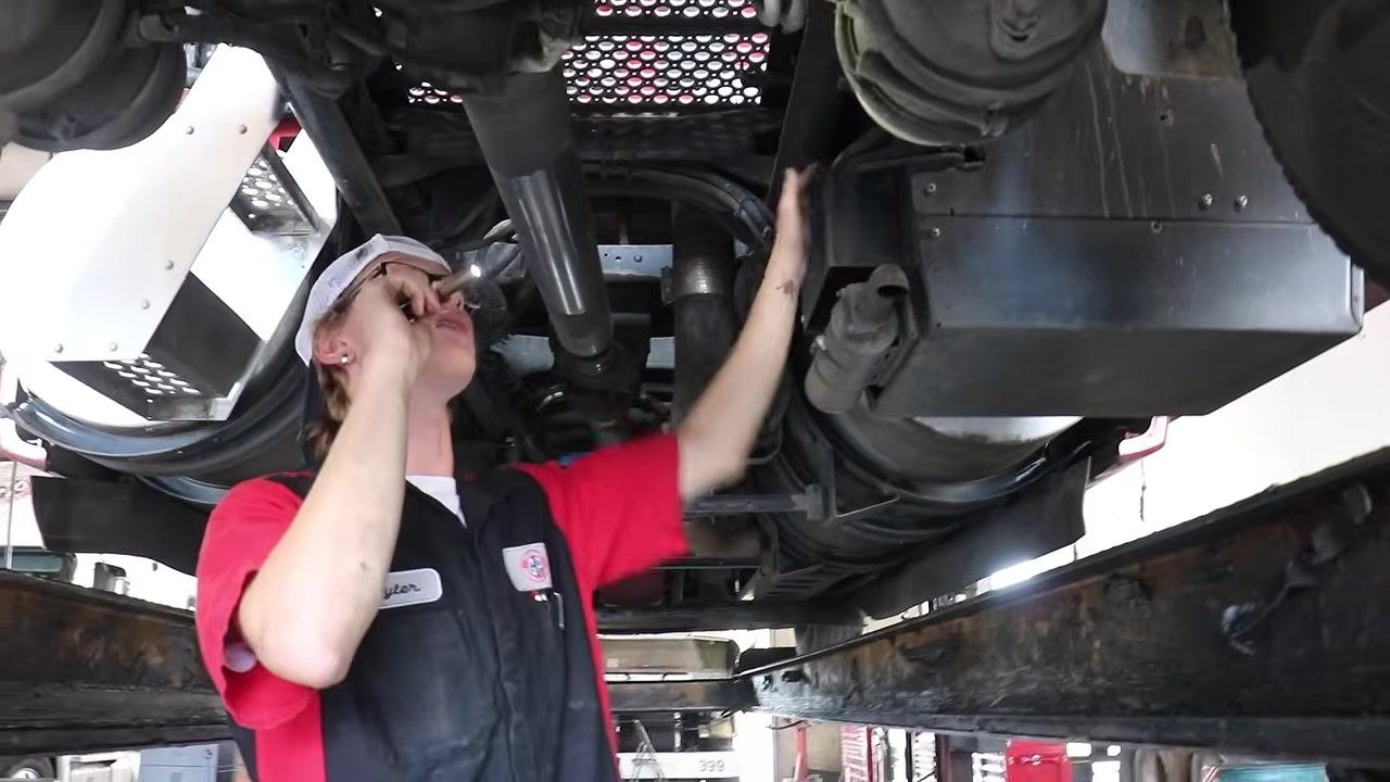 Technician under the truck inspecting the inner wheel rim with a flashlight, checking for rubbing or holes.