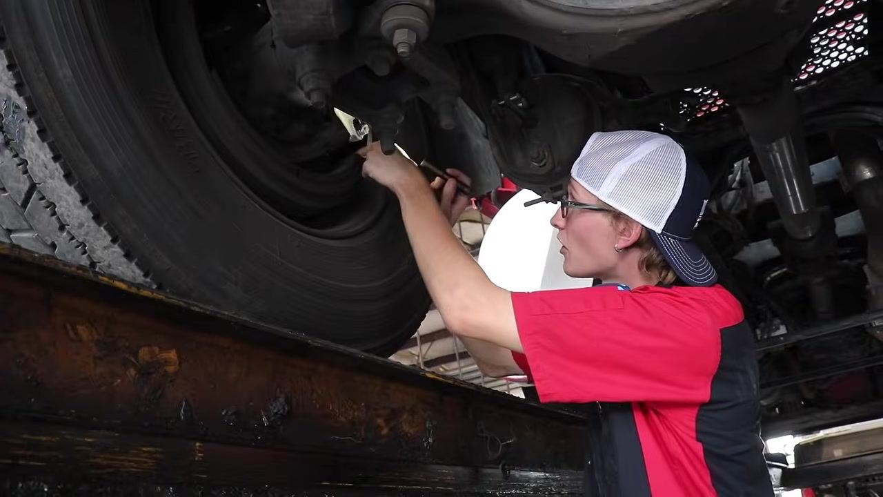 Technician inspecting the brake drum and wheel seal area with a flashlight, checking for cracks or leaks.