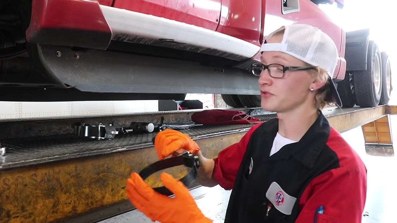 Technician standing beside the truck on the service platform, holding an oil filter wrench, with tools and a rag visible.