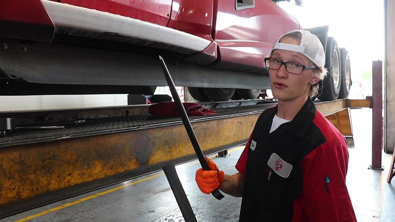 Technician demonstrating the oil filter wrench with both hands, standing beside the truck.