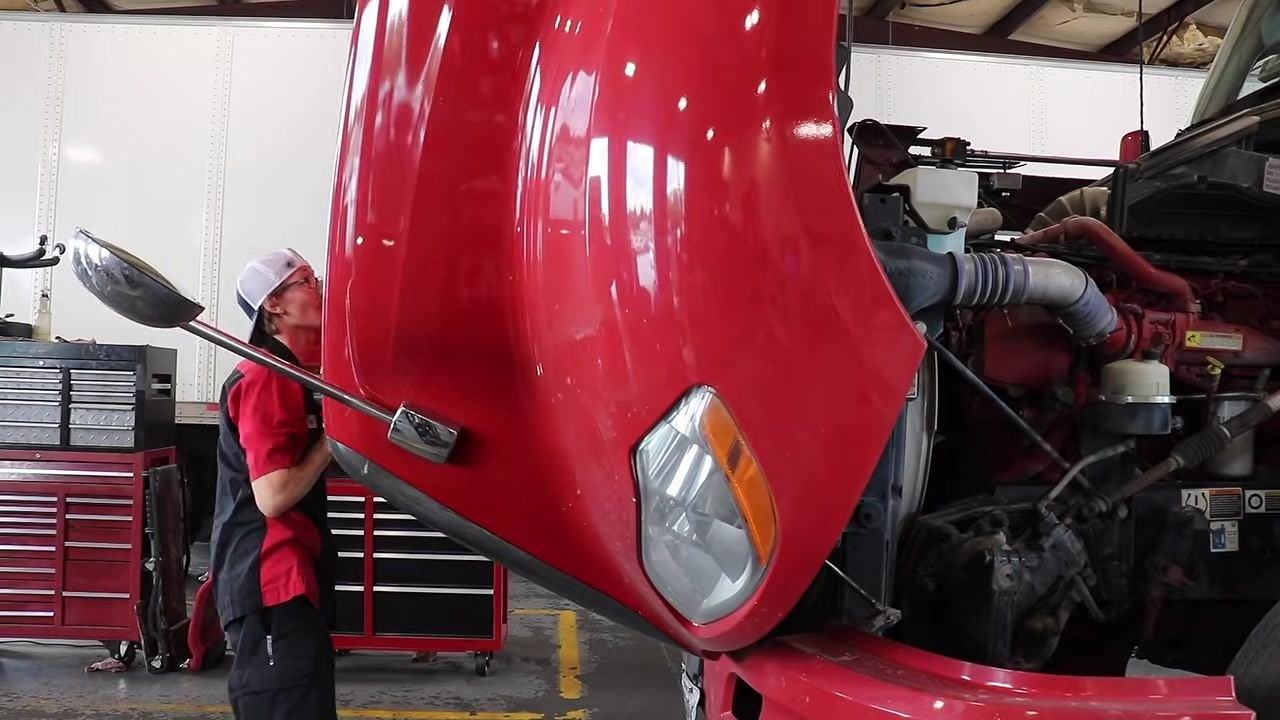 Mechanic pointing at the steering column and power steering reservoir, labeled "Steering Column".