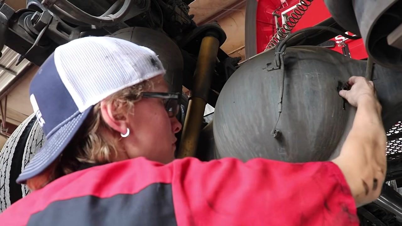 Technician under the truck, wiping hands and cleaning up, with a waste bin containing a used filter in the foreground.